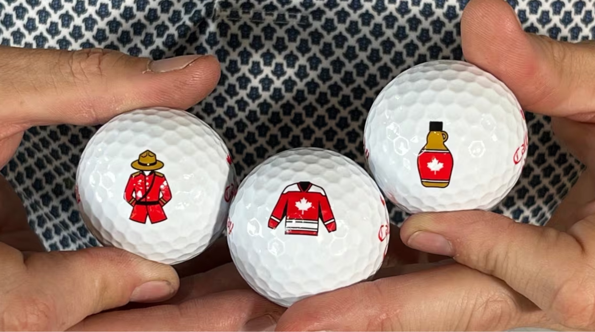 Three golf balls with Canadian-themed designs held by hands.