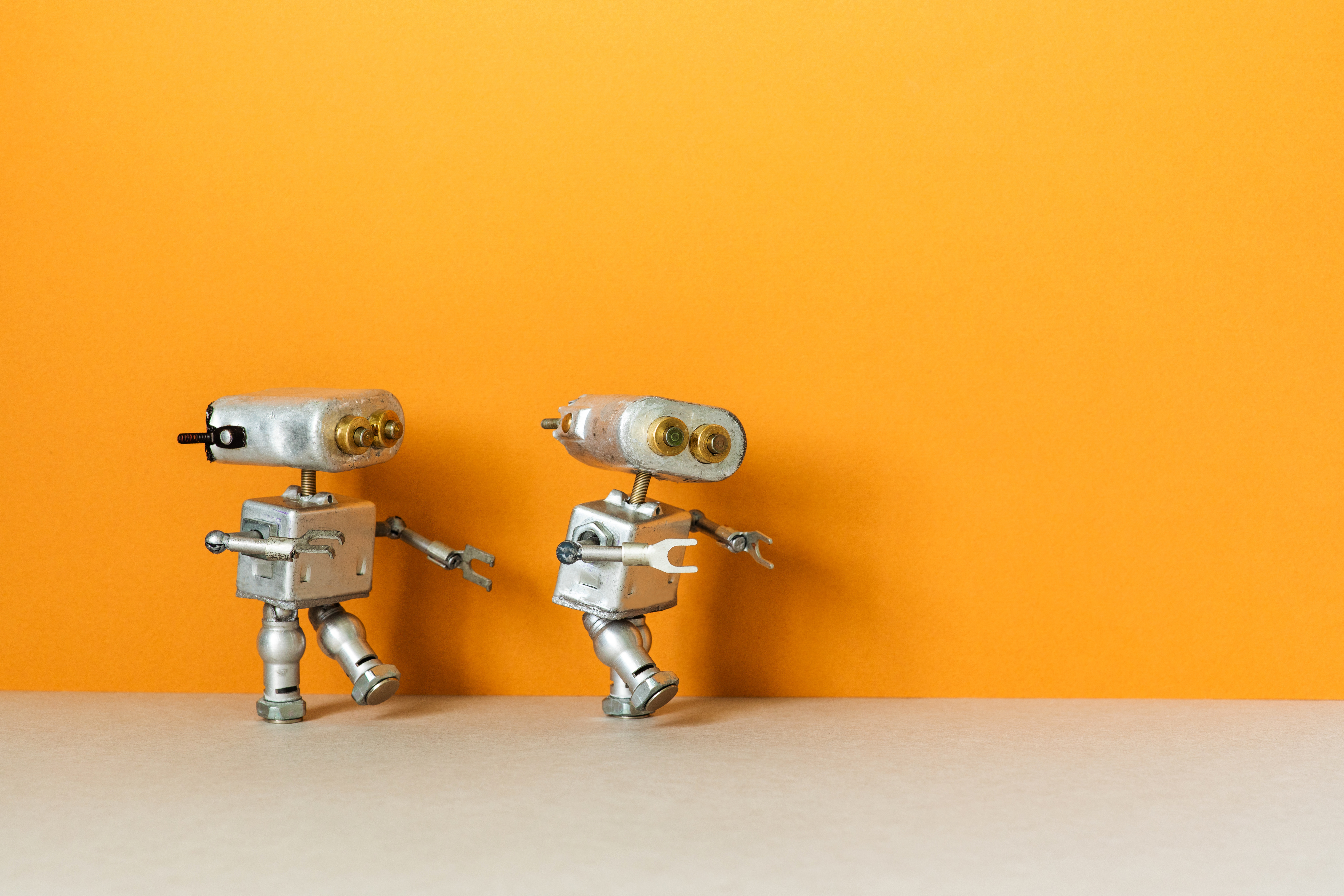 Two small silver robots with bolt eyes on an orange background.