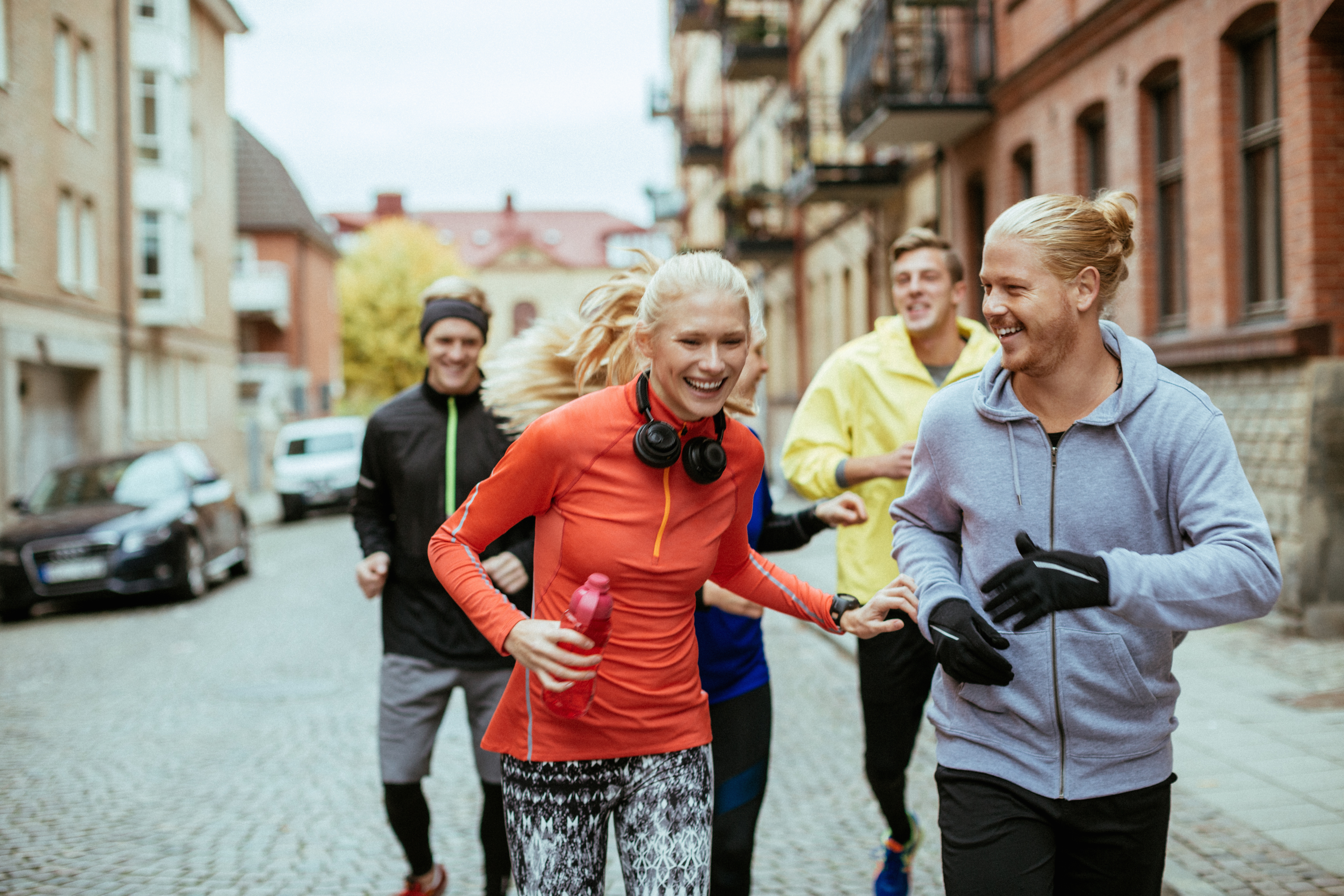 Group of friends jogging on a city street, smiling and cheerful.