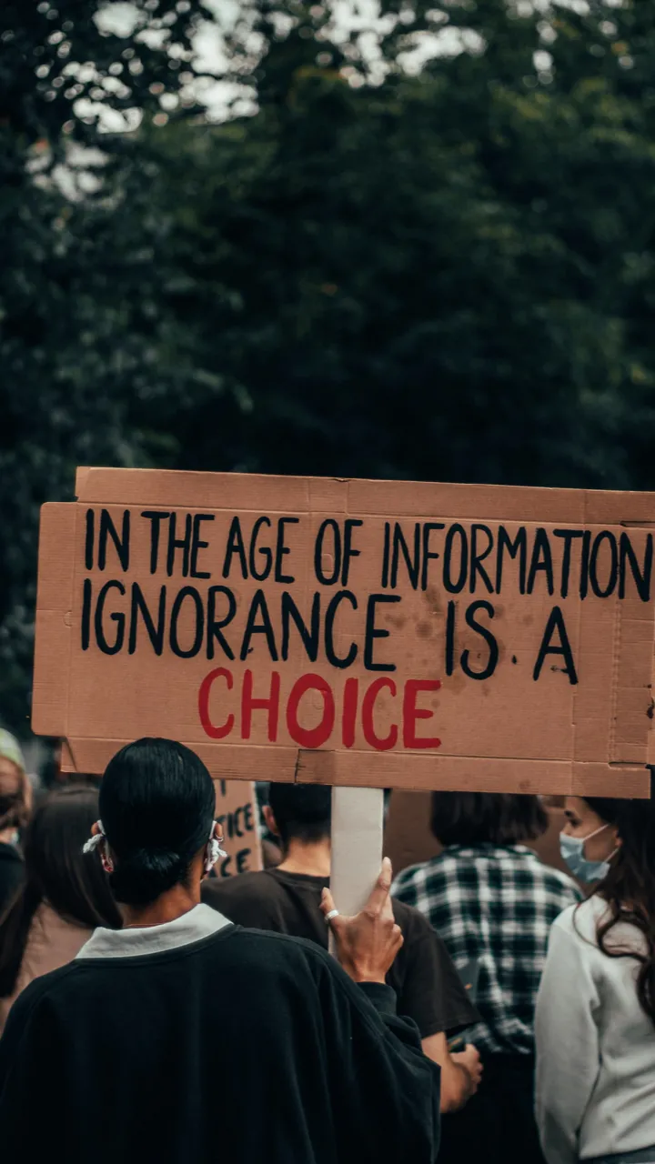 People protesting, holding a sign saying "In the age of information, ignorance is a choice"