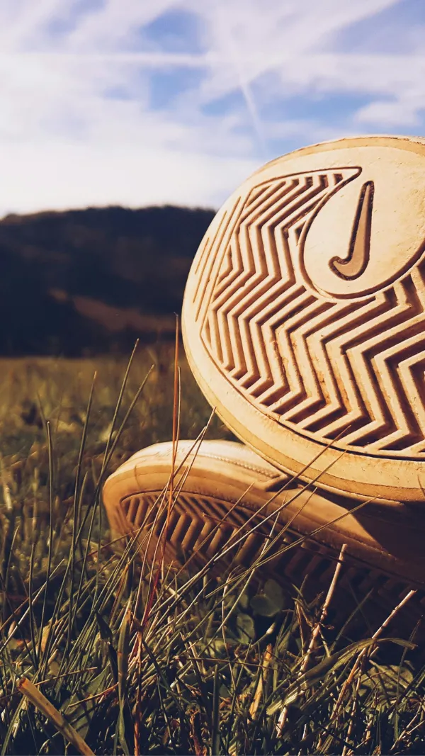 Soles of Nike sneakers with zigzag patterns on grass, under a blue sky.