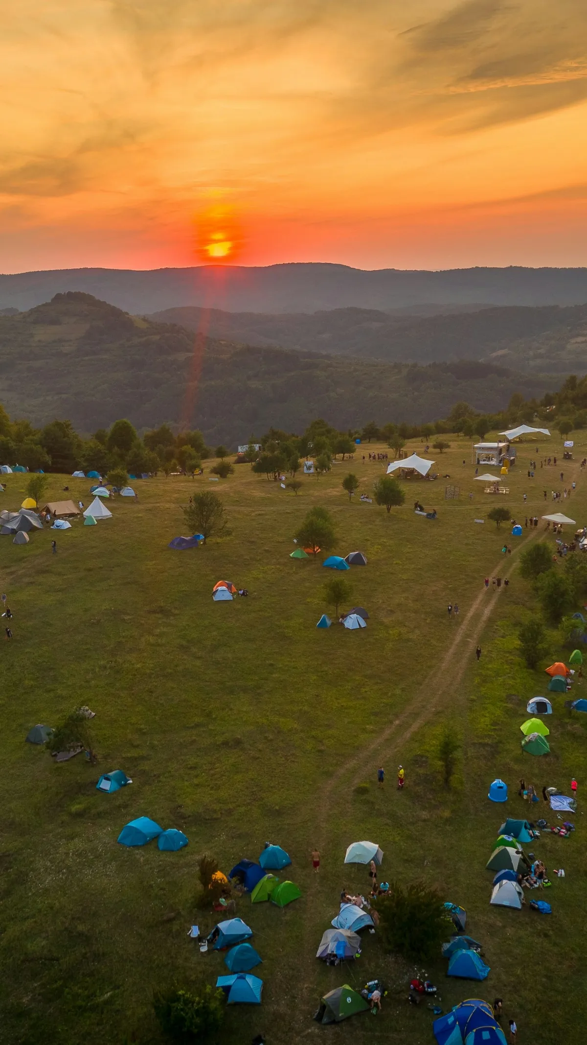Campsite on a grassy hill at sunset with tents scattered around.