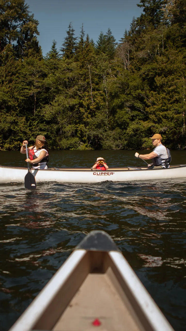 Canoe with three people paddling on a lake surrounded by trees.