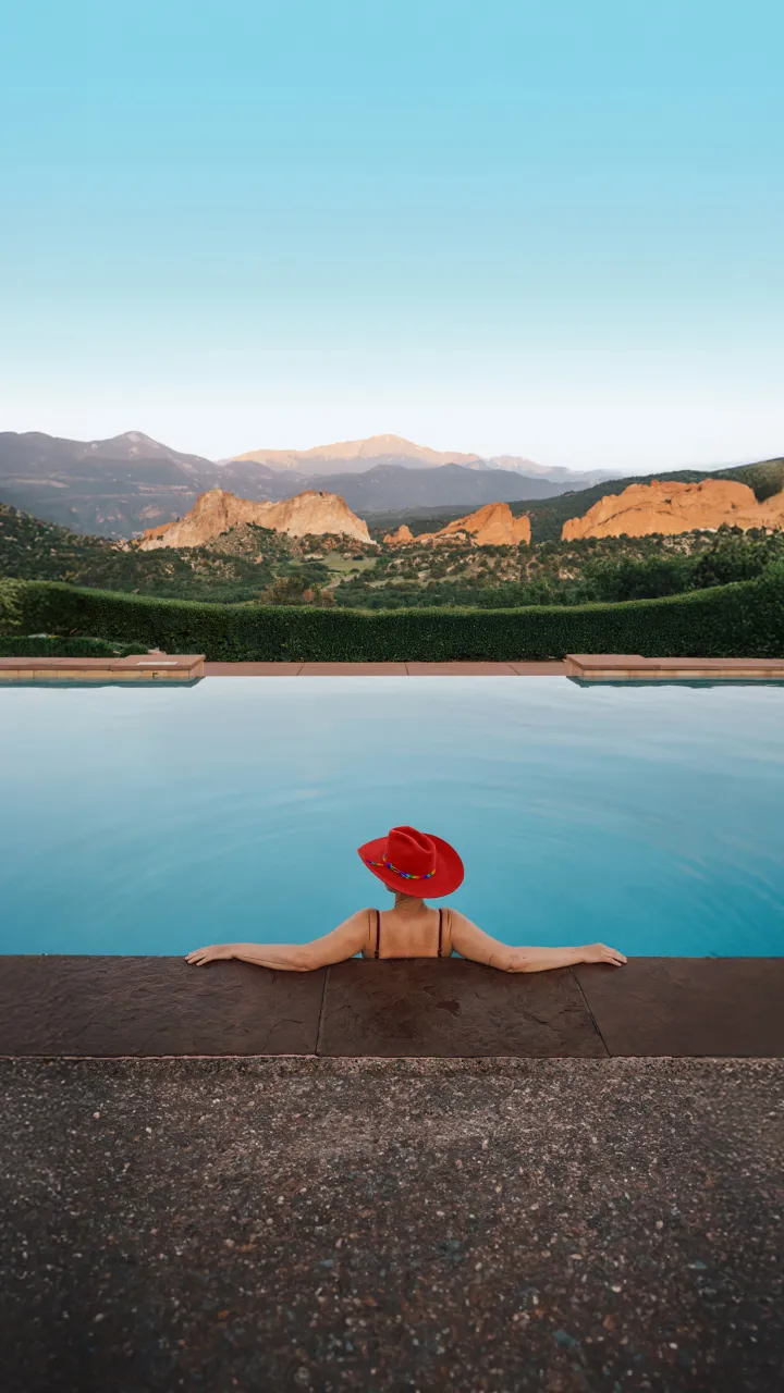Person in a red hat relaxing in an infinity pool with mountain view.