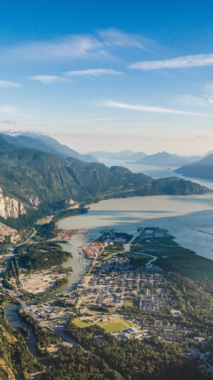 Aerial view of a coastal town, surrounded by mountains and sea under a clear blue sky.