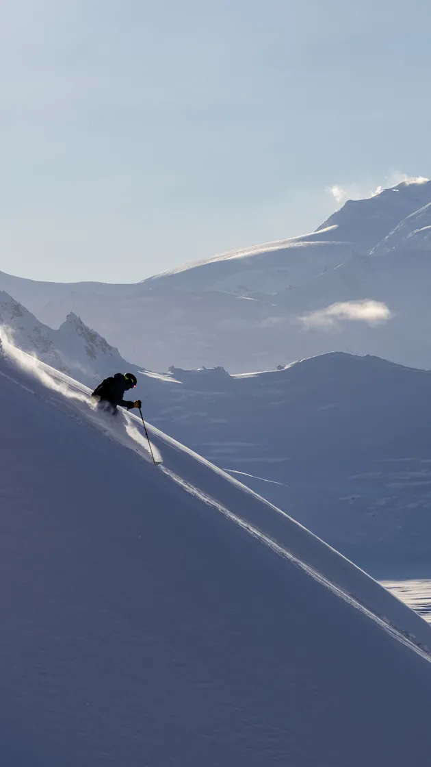 Skier gliding down a snowy mountain slope under a clear blue sky.