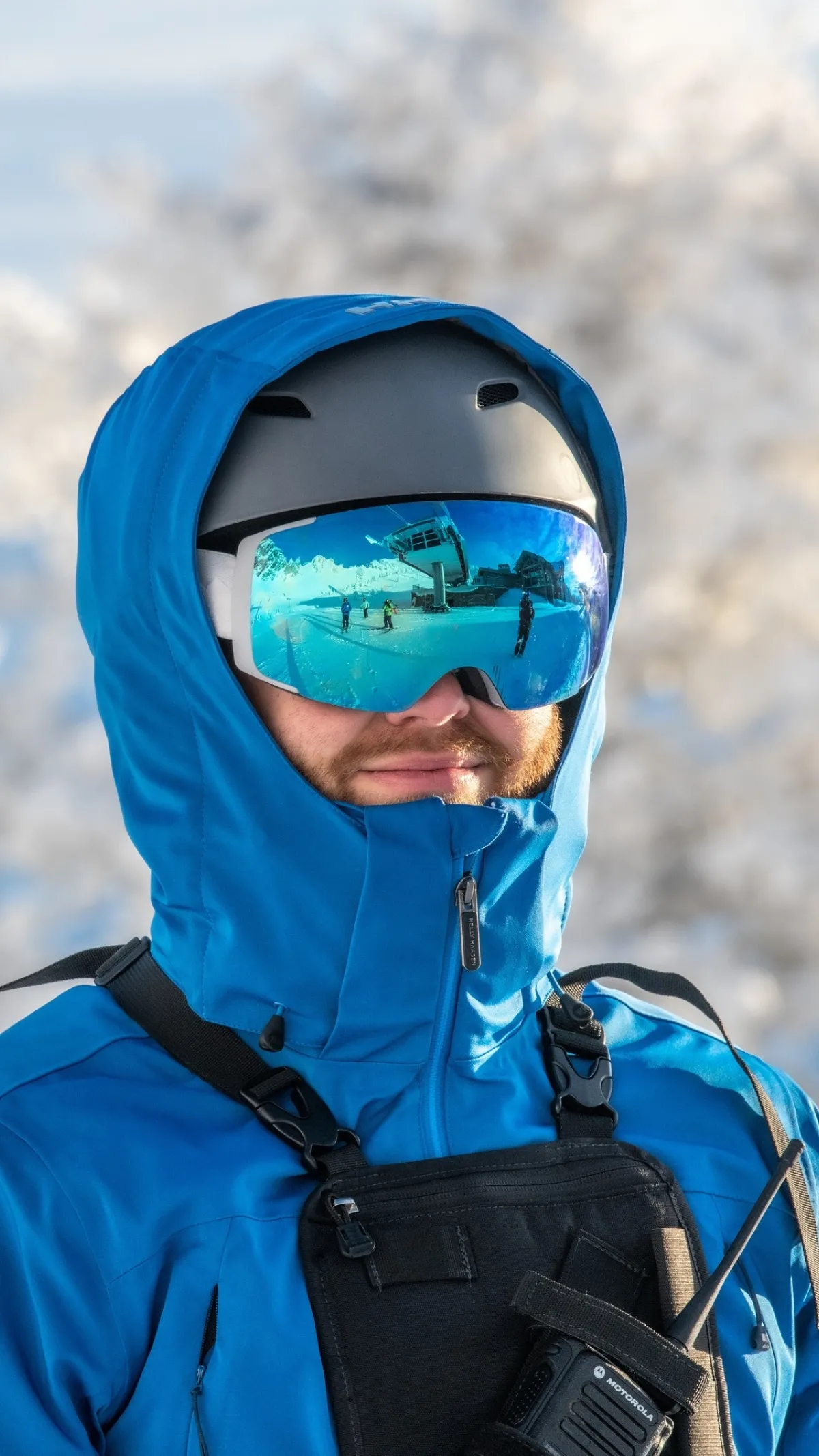 Person in blue ski jacket and helmet, wearing reflective goggles.