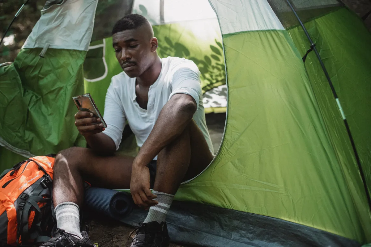 Man scrolling on phone while sitting outside tent