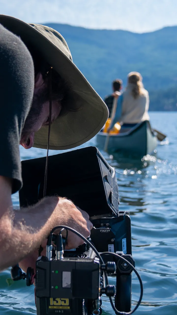 Someone filming 2 people in a canoe on a lake