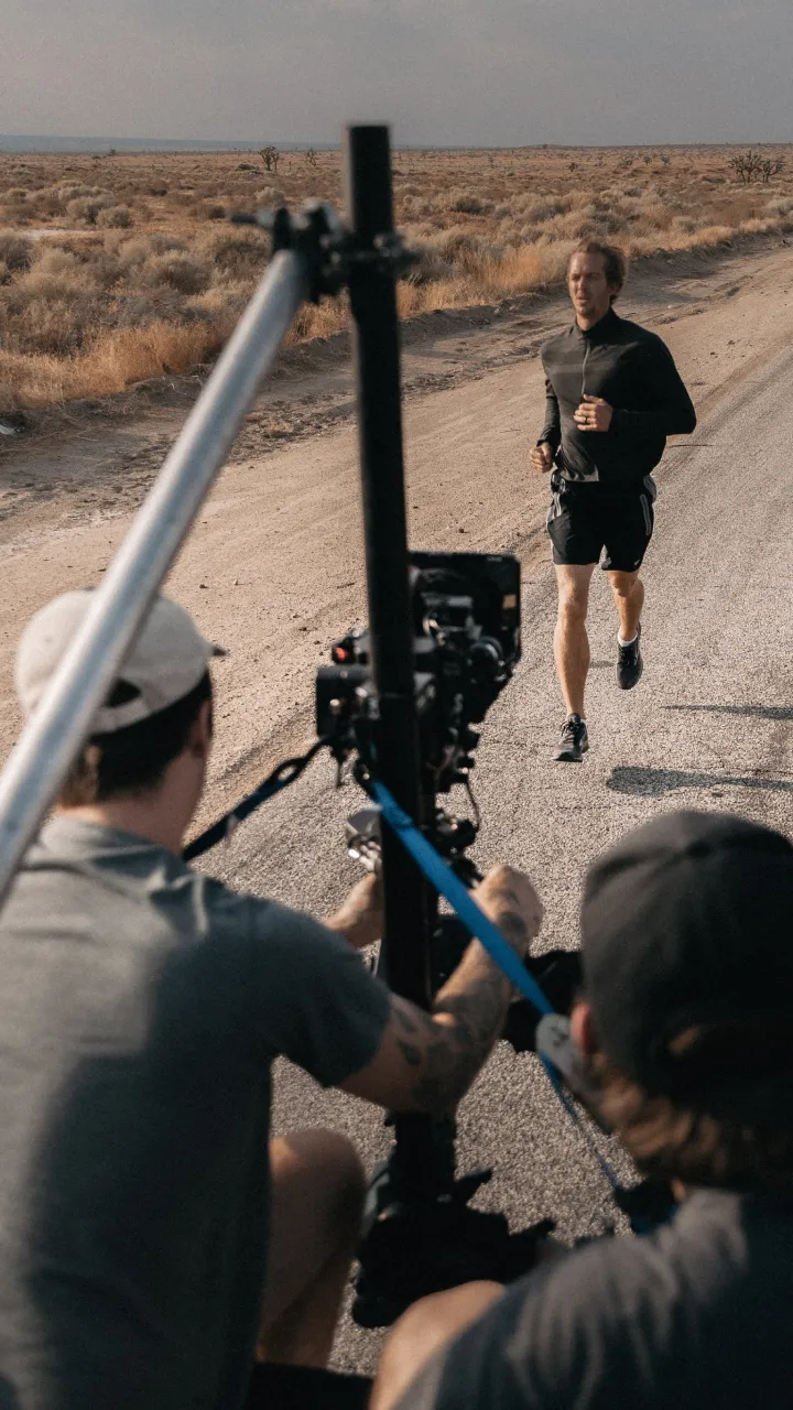 A person running along a road while being filmed by a video crew