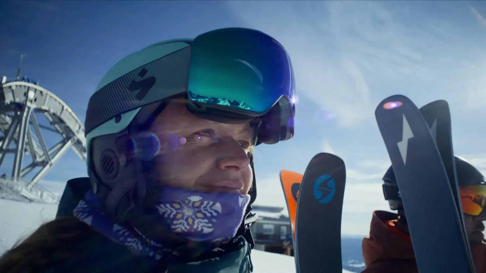 Skier in helmet and goggles on a snowy mountain, skis in hand.