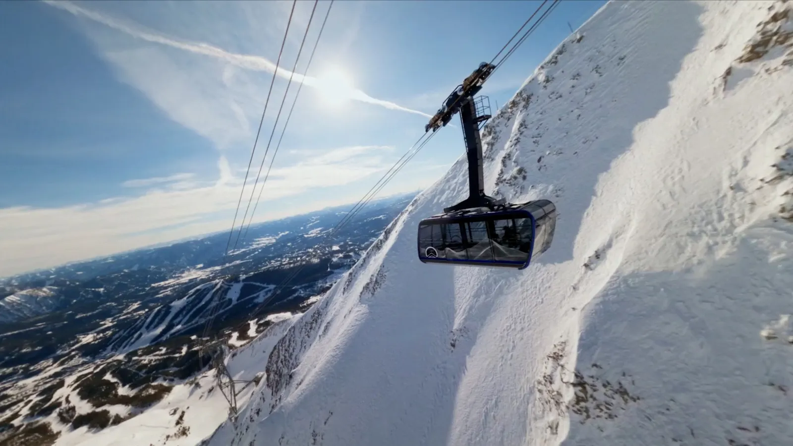 Cable car ascending snowy mountain under clear blue sky.