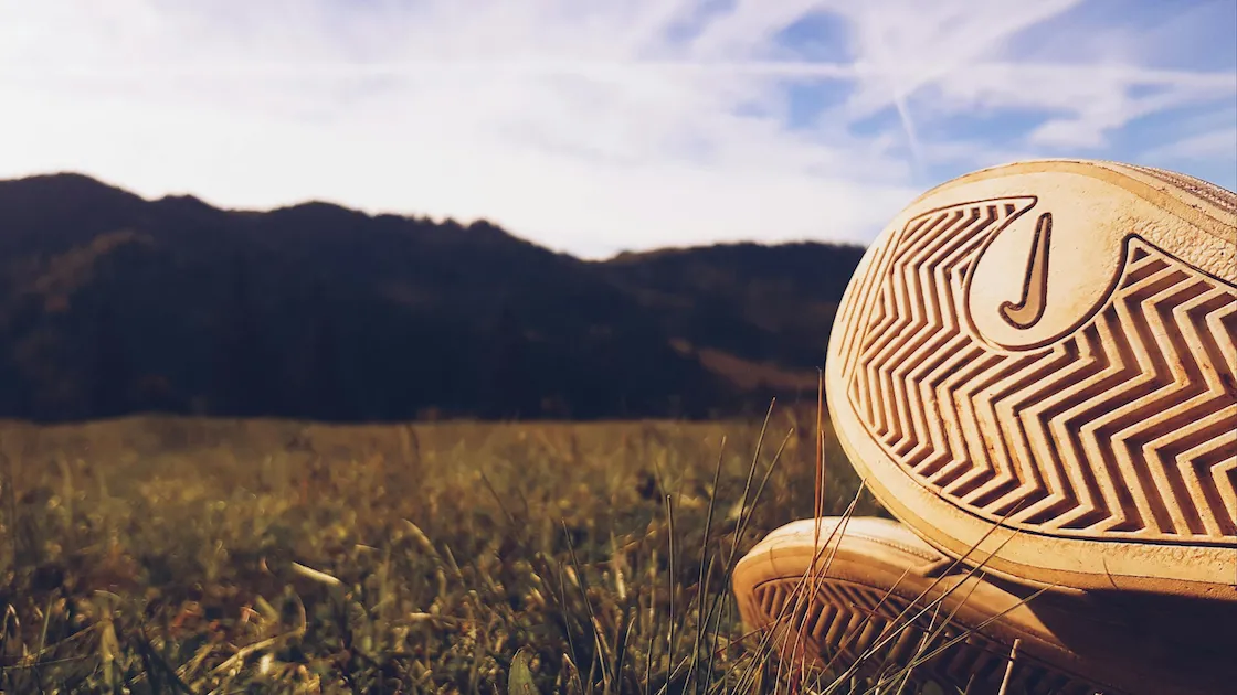 Shoe soles on grass with mountains in the background under a blue sky.