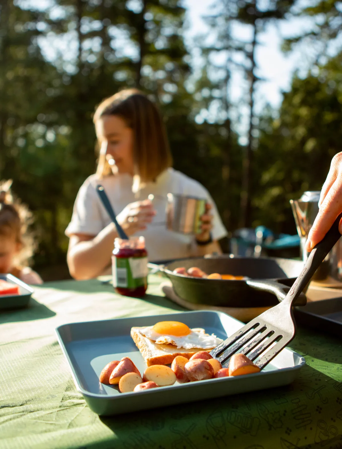Breakfast outdoors, focus on a plate with eggs and potatoes, people in the background.