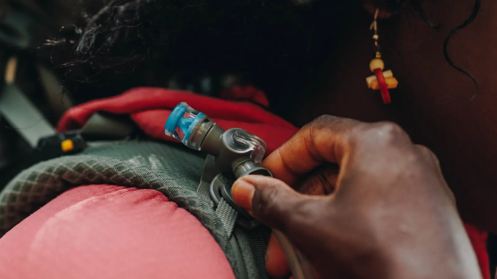 A person's hand holding the comet bite valve on pack strap