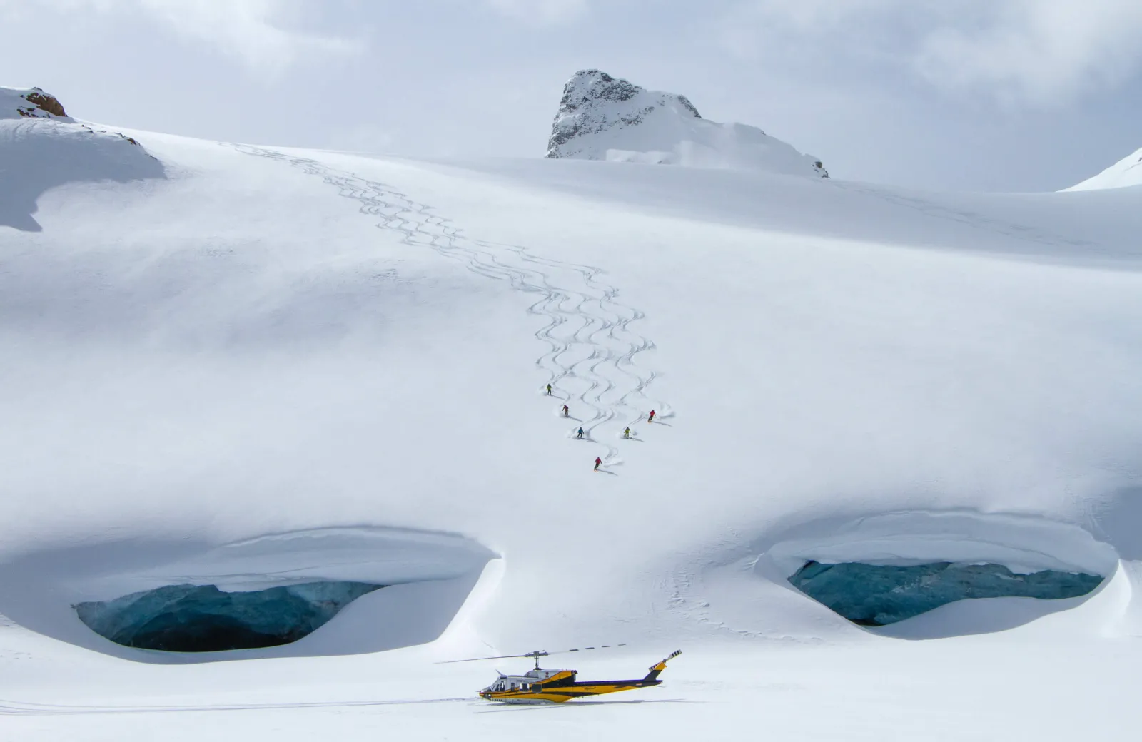 Wide shot of people skiing down to a helicopter