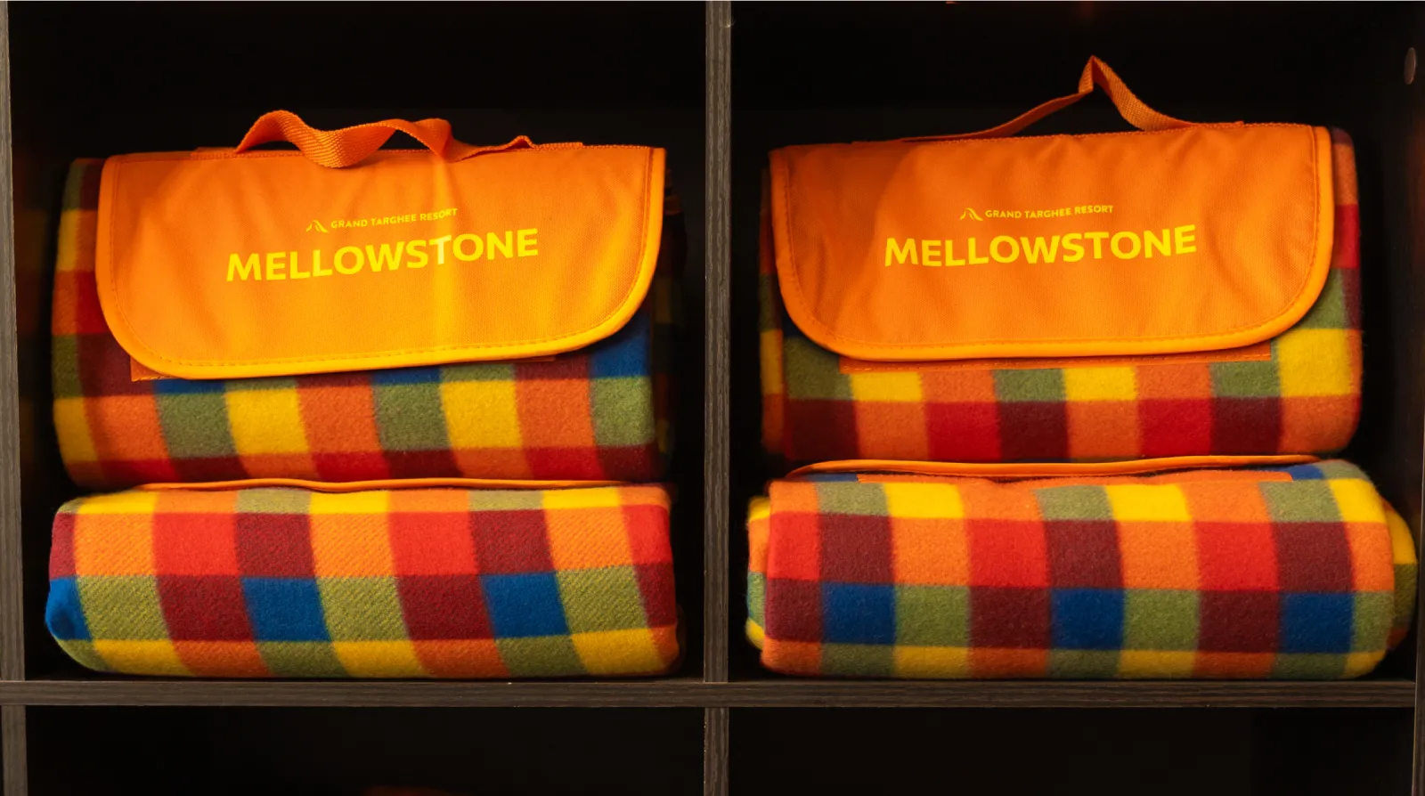 Colorful plaid blankets on a shelf with orange bags labeled "Mellowstone."