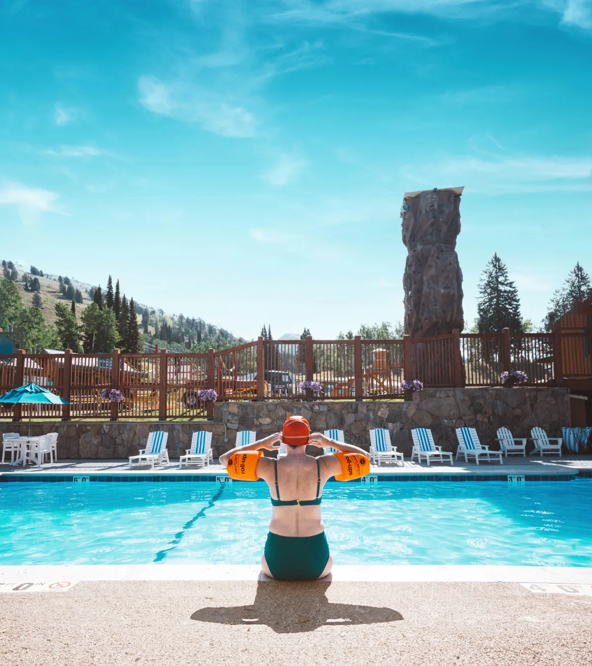 Person sits at the edge of a pool with a mountain backdrop.