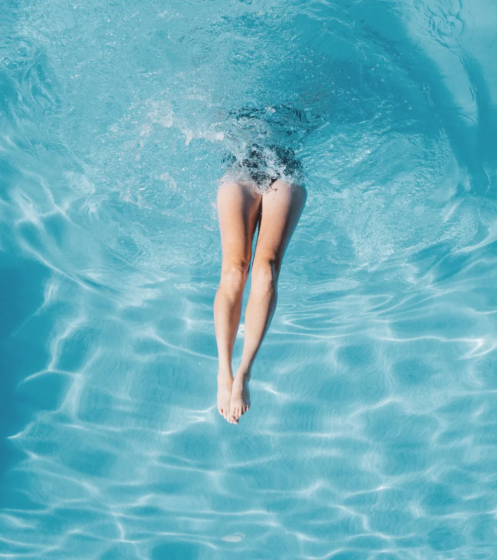 Legs of a person diving into a clear blue swimming pool.