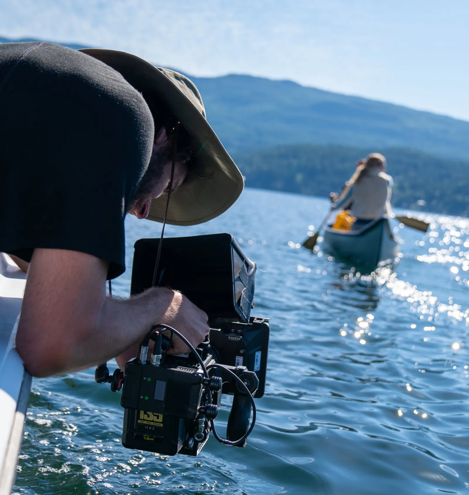 Camerman leaning out of a boat filming people in a canoe