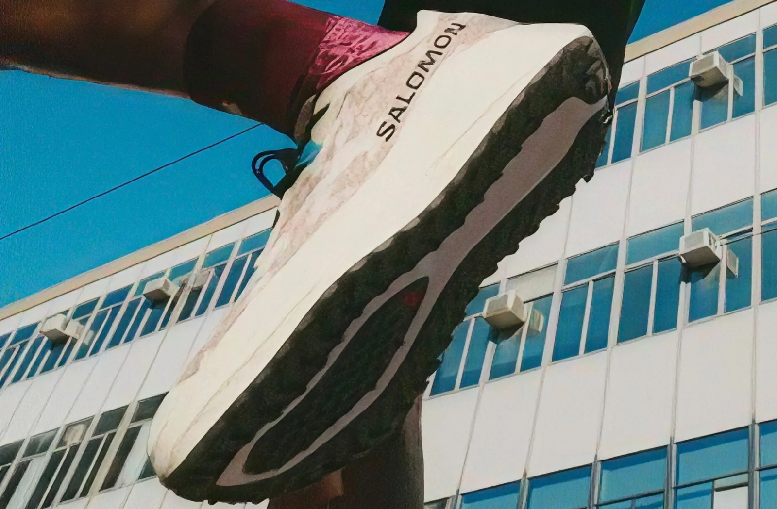 Sneaker with a pink sock, building in the background.