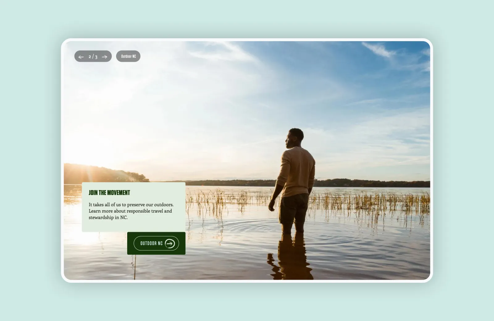 Man standing in shallow water, gazing at sunset over a serene lake.
