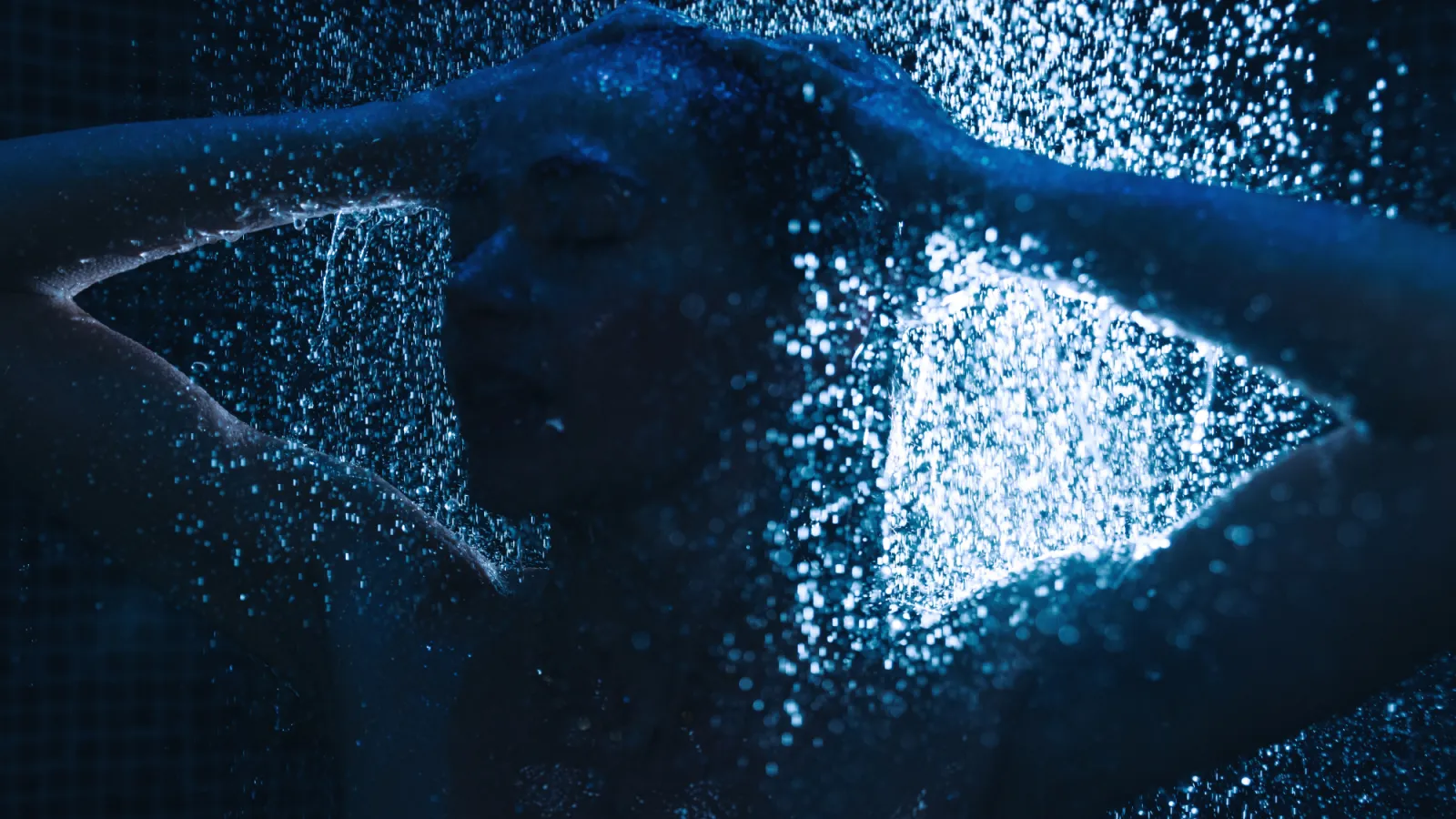 Person standing under blue-lit shower, water droplets falling.