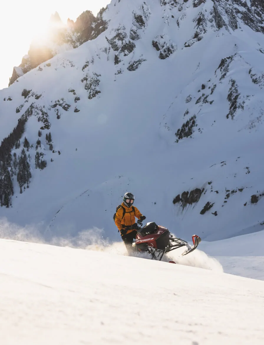 Person riding a taiga snowmobile at sunset