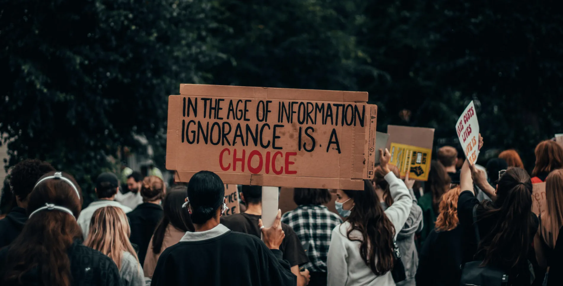People protesting, holding a sign saying "In the age of information, ignorance is a choice"