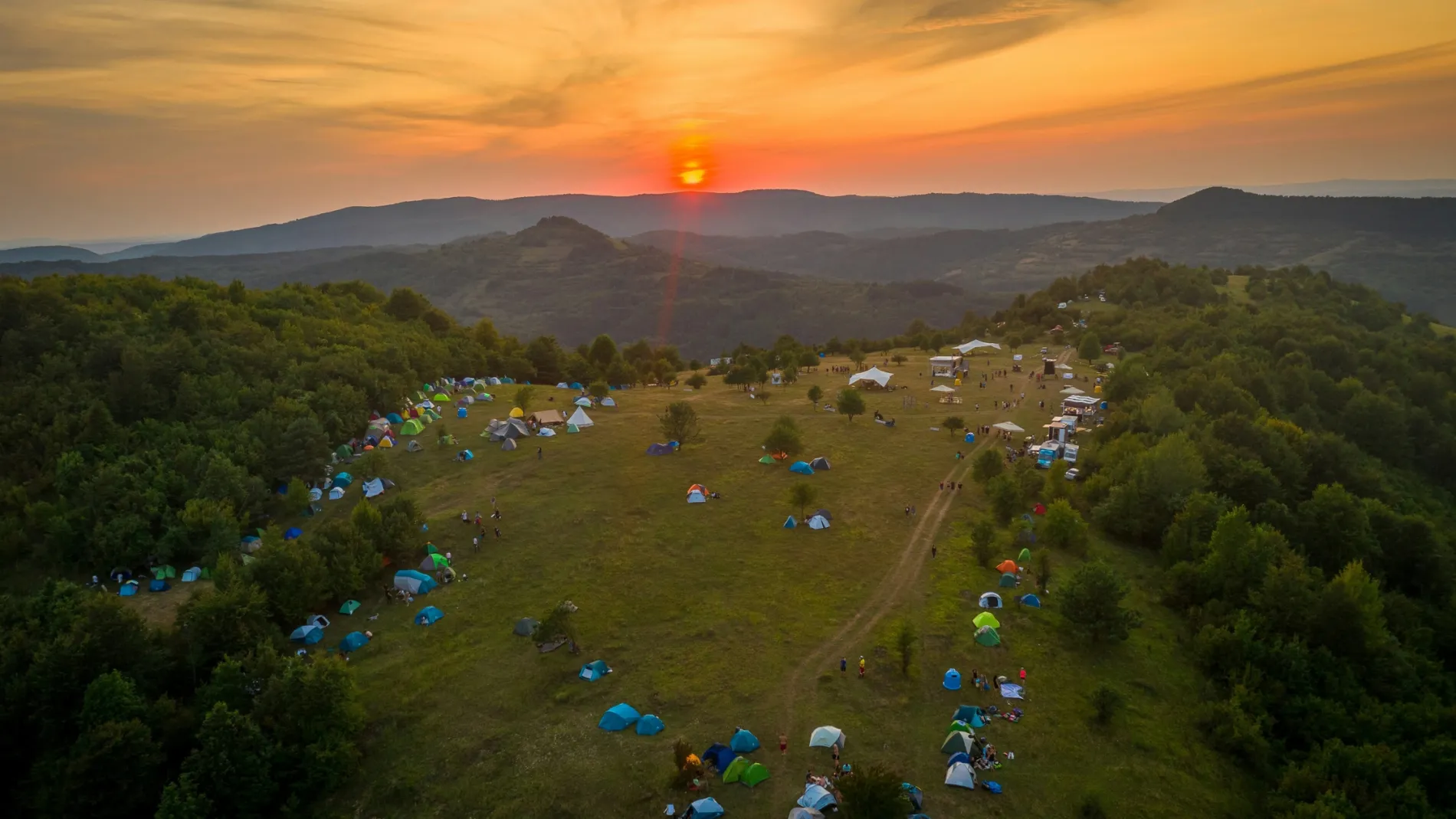 Tents scattered on a hillside at sunset with a distant mountain view.