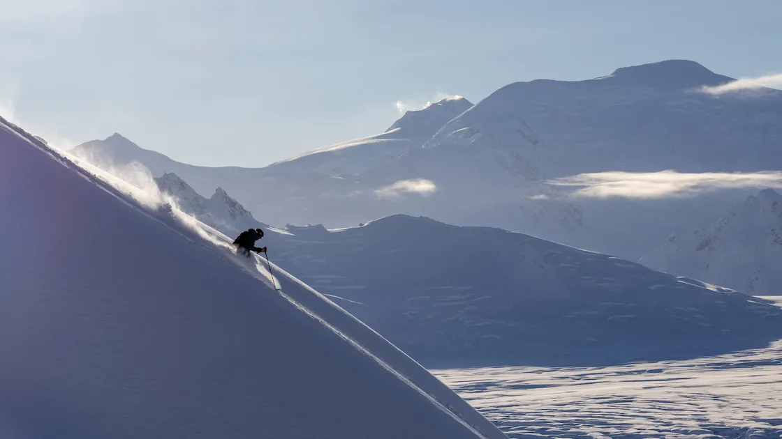 Skier descending a snowy mountain slope against a backdrop of misty mountains.