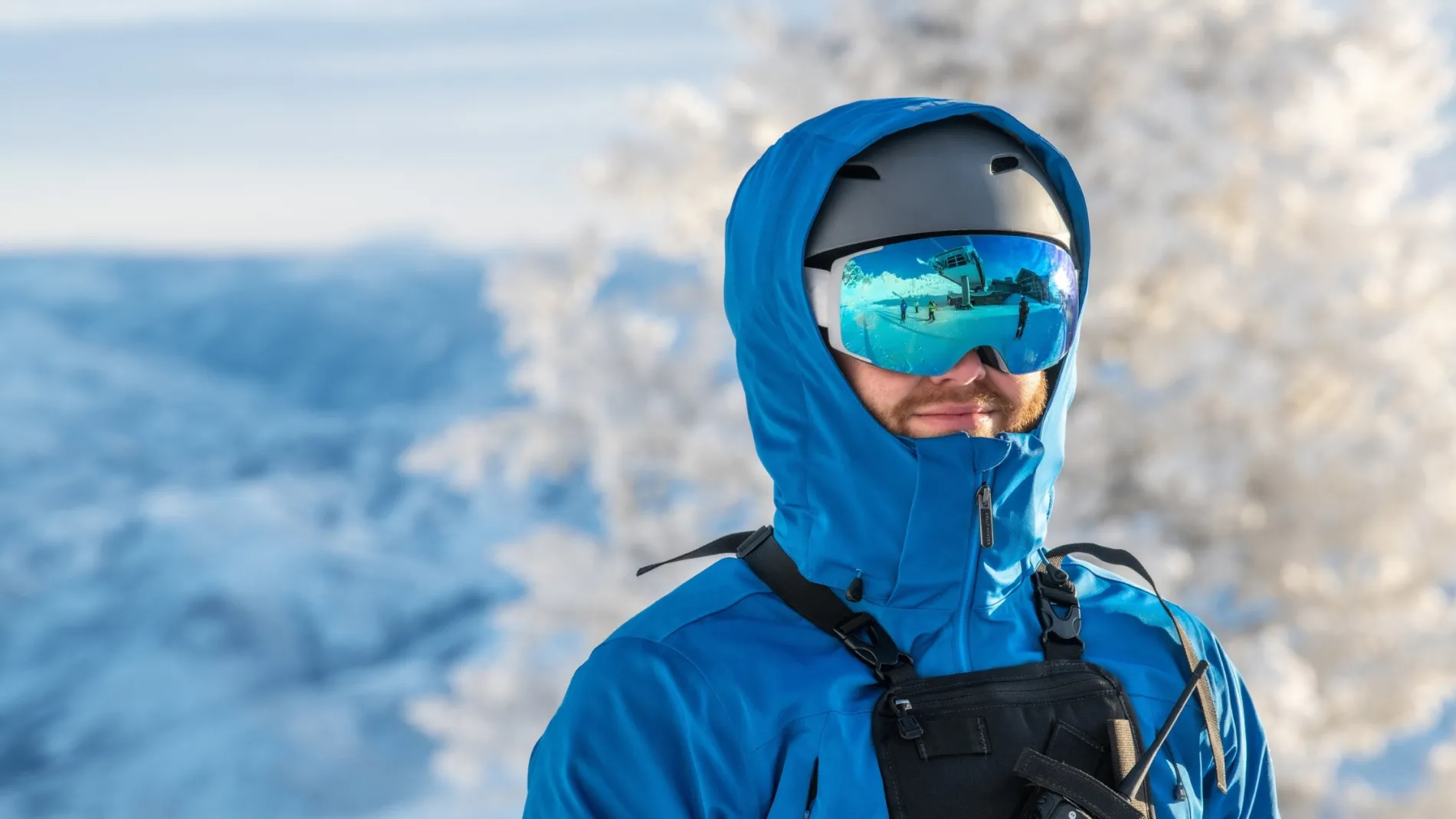 Snowboarder in blue gear and goggles, snowy mountains in background.